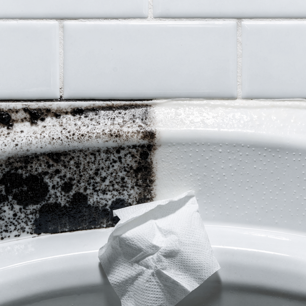 Bathroom caulk seam half stained black and half wiped clean white