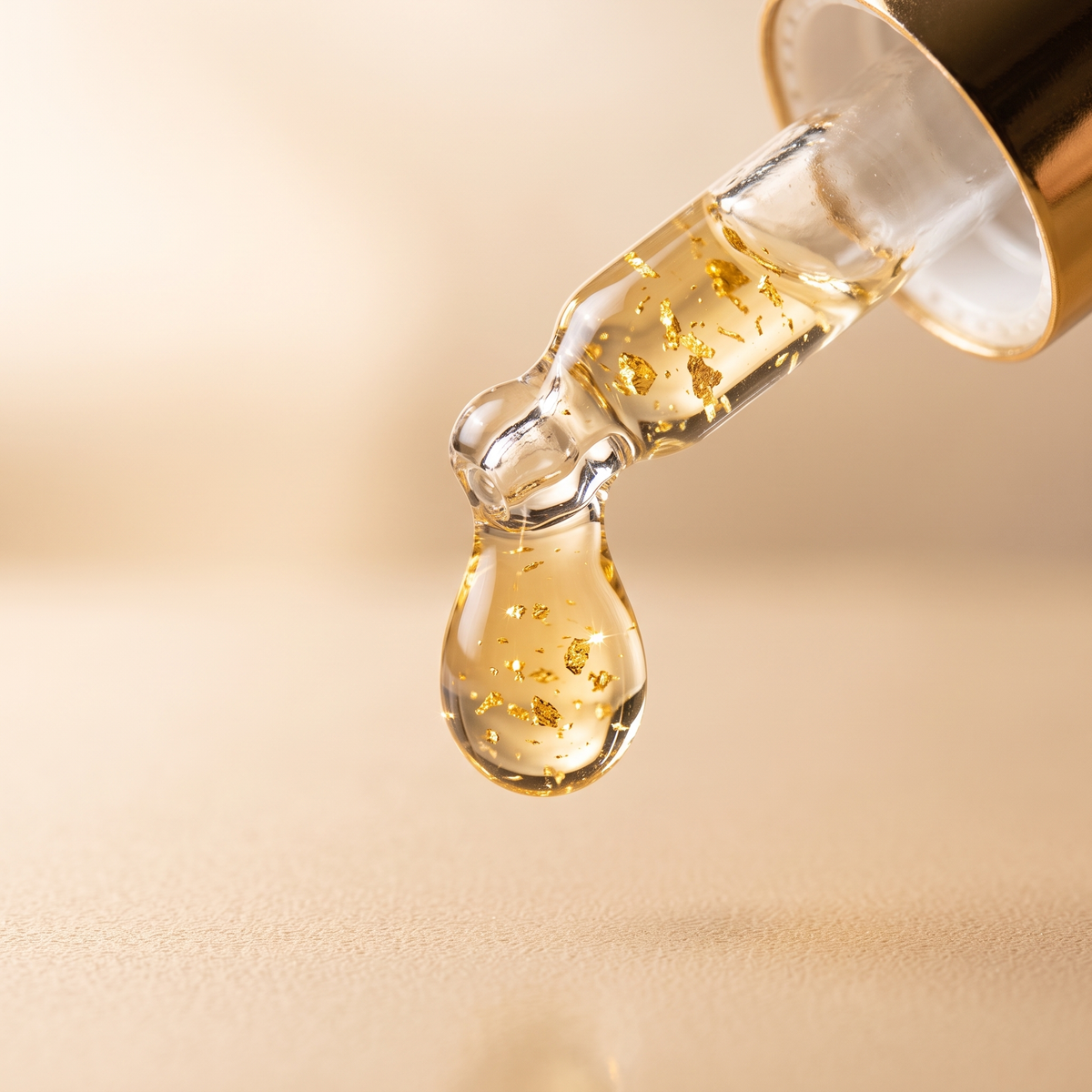 Macro of the GOLD-01 dropper releasing a golden serum drop with visible gold flecks